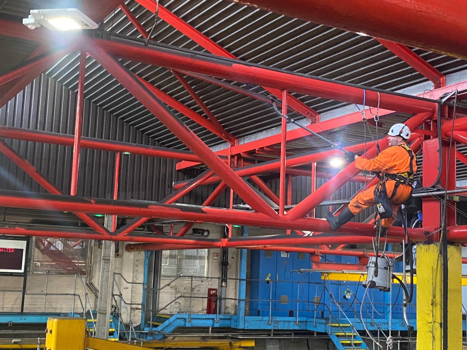 Technician in a harness cleaning a high-level beam inside a factory